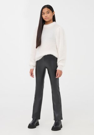 Maglione bianco morbido, pantaloni neri in ecopelle e stivali neri chunky. Design semplice, texture soffice e silhouette aderente.