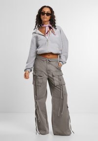 Grauer cropped Reißverschluss-Hoodie mit gesticktem Text, kombiniert mit lockeren grauen Cargo-Hosen, die über mehrere Taschen und eine Kordelzugdetails verfügen.
