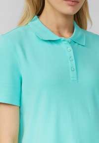 Polo shirt turchese con una texture morbida, colletto e placca con quattro bottoni. Maniche corte e vestibilità rilassata, ideale per un abbigliamento informale.