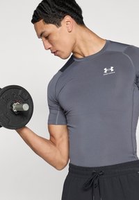 Γκρι αθλητική κοντομάνικη μπλούζα με στενή εφαρμογή, που διαθέτει λογότυπο στο στήθος και υφασμάτινο μοτίβο στον ώμο, συνδυασμένη με μαύρο σορτς.