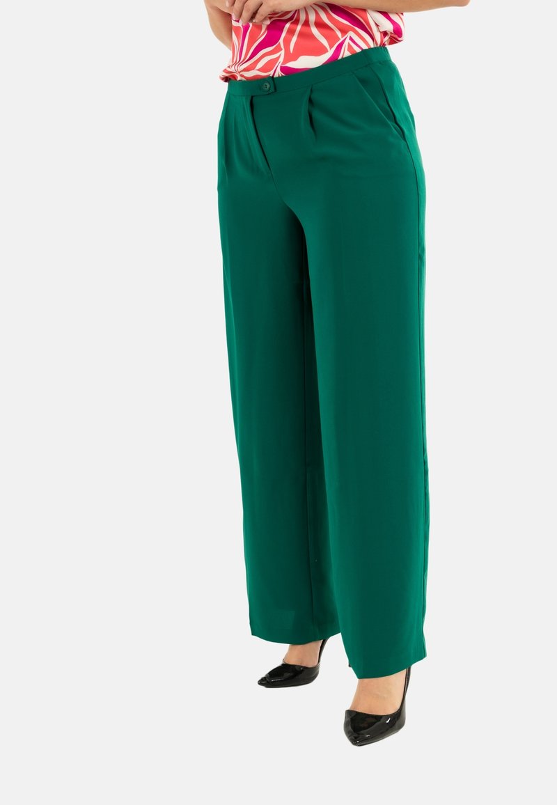 Pantalones verdes de pierna ancha con una textura suave y fluida, con plisados frontales y un cierre de botón, combinados con tacones de punta negra.