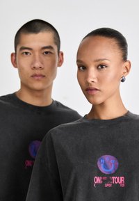 Gray oversized short-sleeve shirts feature colorful graphic designs, including a smiley face and text, against a soft, textured fabric.