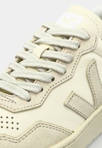 Baskets avec une tige en cuir crème et des accents en suède beige. Elles présentent des lacets texturés, des détails perforés et un patch logo sur la languette.