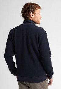 Suéter azul marino con un patrón texturizado, cuello elevado y puños acanalados. Presenta un ajuste holgado y está hecho de un material suave.