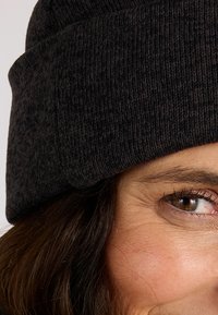 Gorro de lana negro con un patrón texturizado, con puño vuelto y acabado suave. Primer plano de una cara, mostrando un tono de piel cálido y un ojo marrón.