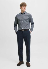 Cămașă modelată de culoare bleumarin cu nasturi, mâneci lungi și guler clasic, asortată cu pantaloni bleumarin și pantofi maro închis.