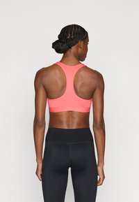 Koraalrode sportbeha met racerback-ontwerp, gemaakt van gladde stof, gecombineerd met hooggetailleerde zwarte legging. Naadloos en nauwsluitend ontwerp.