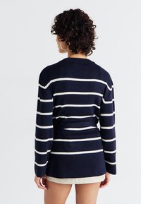 Sweater azul-marinho com riscas horizontais brancas, mangas longas e um corte solto. Textura suave e um decote arredondado com uma cintura cinto.