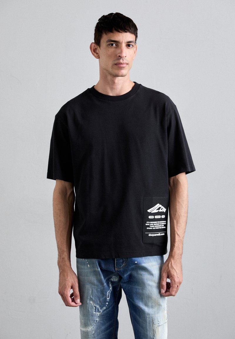 Black oversized t-shirt in cotton, featuring a white graphic pocket detail and short sleeves. Paired with distressed blue jeans.