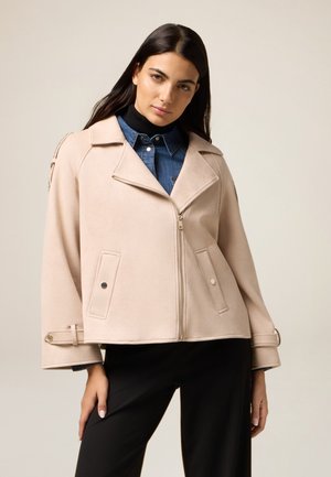 Veste en tissu doux de couleur rose clair, avec zip à l'avant, col large et poches. Offre une coupe décontractée et des boutons décoratifs sur les manches.