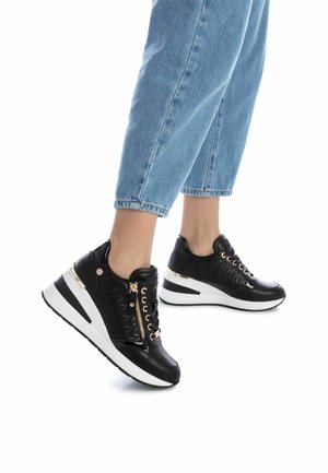 Zapatillas de cuero negro con un acabado texturizado, detalles en dorado y una suela cuña blanca. Cuentan con un cremalleras lateral y detalles de cordones.
