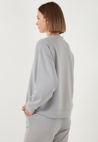 Sudadera gris claro con un corte relajado, textura suave, hombros caídos y un escote amplio. Diseño simple sin patrones o acentos visibles.