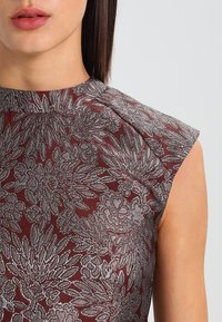 Burgundská květinová šaty s metalickými stříbrnými listovými vzory, krátkými rukávy a texturovanou tkaninou. Vybaveny vysokým výstřihem a strukturovanými rameny.