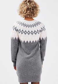 Robe pull grise en tricot avec manches longues, présentant un motif géométrique blanc neige et rose pâle sur l'empiècement. Matière douillette et longueur jusqu'aux hanches.