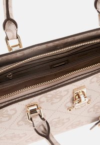 Sac à main beige avec un motif de logo, texture lisse, plusieurs compartiments, quincaillerie dorée et une sangle amovible. Fermeture zippée.