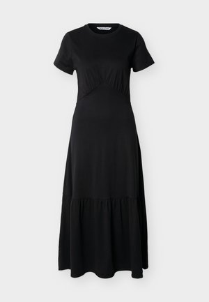 Μαύρο μακρύ φόρεμα με κοντά μανίκια, στρογγυλή λαιμόκοψη, ραφή στη μέση που δημιουργεί πτυχώσεις και φούστα με στρώσεις, σε απλό ανοιχτό φόντο.