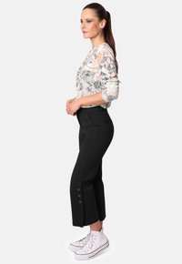 Pantalones cortos negros con acentos de botones en el dobladillo, combinados con una camisa de manga larga estampada en colores suaves y claros y zapatillas altas blancas.