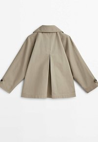 Beige värinen lyhyt takki, jossa pitkät hihat, napitetut kalvosimet, keskellä takana laskos ja leveä, teräväkaulainen kaulus.