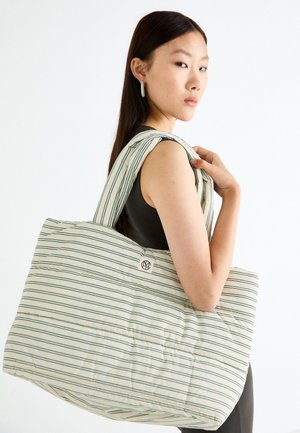 Striped fabric tote bag in soft, padded material. Features a large body with a round logo and wide, striped straps.