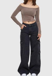 En axelbandslös glittrig brun crop top ihop med svarta vida cargobyxor med sidofickor och sönderriven nederkant. Vita sneakers.