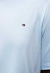 Ανοιχτό μπλε βαμβακερό μπλουζάκι με μικρό ορθογώνιο λογότυπο σε ναυτικό μπλε, λευκό και κόκκινο στο πάνω μέρος του στήθους.