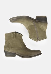 Botas cortas de tobillo en ante verde oliva, con una cremallera en un lado, tacón bajo y costuras decorativas en el eje.