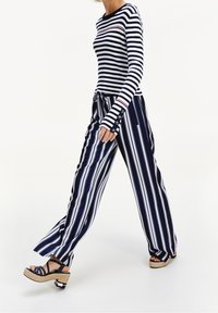 Marineblauw-wit gestreepte top met lange mouwen en rode accenten; gecombineerd met wijde, gestreepte broekspijpen en marineblauwe sleehakken met een espadrillezool.