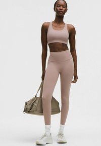 Bustieră sport roz deschis și colanți înalți asortați din material elastic, purtați cu șosete albe până la gleznă și încălțăminte sport deschisă la culoare.