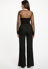 Zwart bodysuit met doorschijnende lange mouwen met stippen, gecombineerd met zwarte hoge taille wijde pantalons en ingewikkelde kanten manchetten.