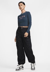 Top Nike navy cropped cu mâneci lungi, cu logo roșu, asortat cu pantaloni cargo negri. Adidași Nike negri și albi cu șireturi.