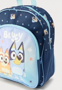 Μπλε υφασμάτινο σακίδιο πλάτης με κινούμενους χαρακτήρες στο μπροστινό μέρος, σχέδια με αστεράκια, διπλά φερμουάρ και ανοιχτό μπλε λεπτομέρειες· συμπαγές σχέδιο.