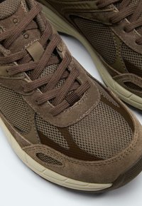 Brown athletic sneakers with mesh and suede panels, thick beige soles, and matching brown laces, shown close-up and side by side.