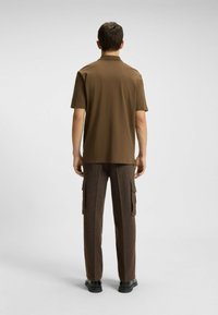 Brązaowa koszula z krótkim rękawem i kołnierzykiem, sparowana z brązowymi teksturowanymi spodniami cargo z kieszeniami bocznymi i prostym krojem. Czarne obuwie.