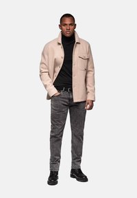 Chaqueta de mezcla de lana beige con cierre de botón, dos bolsillos en el pecho, suéter de cuello alto negro, jeans grises y botas negras con cordones.