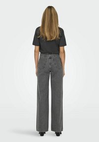 Jeans de mezclilla gris de cintura alta con un corte de pierna ancha, que cuentan con dos bolsillos traseros y costuras de contraste. Combinados con una camiseta negra.