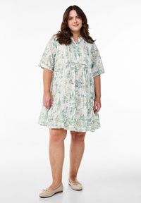 Robe à imprimé floral avec des manches courtes, décolleté en v, ourlet froncé et accents en dentelle ; principalement blanche avec des motifs verts et jaunes.