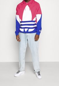 Huvan i rosa, vitt och blått med stor grafisk design; kombinerad med ljusblå denimjeans och vita sneakers med svarta skosnören.