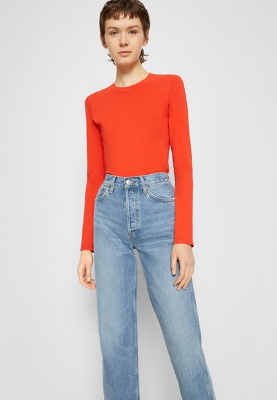 Camisola vermelha de manga longa combinada com jeans de cintura alta de pernas retas em azul claro. A camisola tem um decote redondo e um design ajustado, enquanto os jeans apresentam o clássico estilo de cinco bolsos.