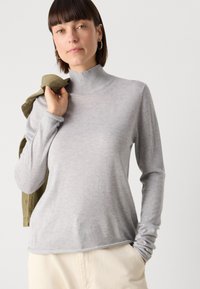 Svijetlosiva turtleneck majica dugih rukava od mekog materijala. Ima prilagođeni kroj i glatku teksturu, s malo opuštenim fitom na rubu.