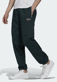Pantaloni jogger neri con polsini elasticizzati, tasca laterale con zip e logo ricamato. Abbinati a sneakers bianche. Design rilassato e morbido.
