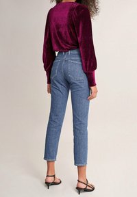 Strakke, hoge taille, blauwe denim jeans met vijf zakken en gestikte details, gecombineerd met een diep bordeauxrood, textuur, langemouwen top.
