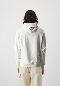 Sudadera de crema clara con capucha y cordón, puños acanalados y una textura lisa y suave. Presenta un diseño minimalista y un ajuste relajado.
