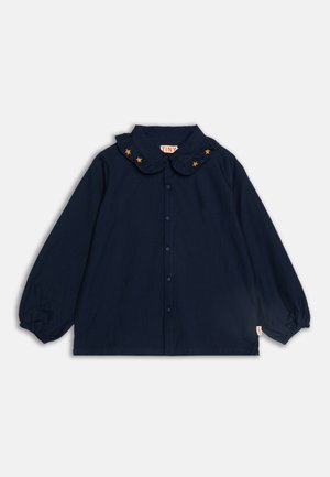 Blouse manches longues bleu marine avec un col volanté orné d'étoiles jaunes ; comporte une fermeture à boutons à l'avant et des poignets élastiques.