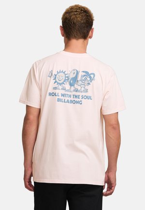 T-shirt en coton rose avec une impression graphique bleue de personnages joyeux et le texte "ROLL WITH THE SOUL BILLABONG" au dos. Manches courtes.