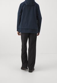 Navy water-resistant jacket with a hood, dropped hem, and long sleeves, paired with black loose-fitting pants and outdoor footwear.