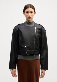 Casaco de couro preto com design curto, fecho de correr prata, bolsos laterais e cintura com cinto. Apresenta um colarinho estruturado e mangas longas.