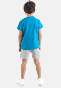 Camiseta de algodón azul, pantalones cortos grises y zapatillas deportivas blancas de caña alta. La camiseta tiene cuello redondo y mangas cortas, con una textura suave.