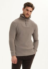 Beige gebreide pullover met hoge kraag en ritssluiting aan de voorkant. Heeft een geribbelde textuur en een vierkant yoke-ontwerp. Slim fit met lange mouwen.