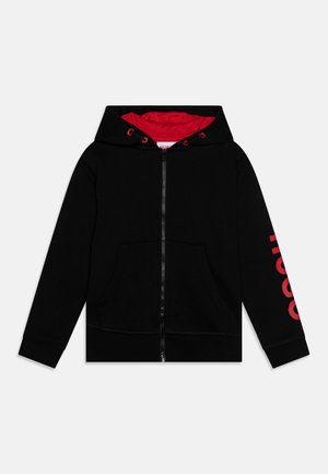 Sweat à capuche zippé noir avec un intérieur rouge et des cordons, présentant une poche avant et un texte rouge en gras sur la manche gauche.