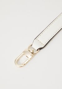 Hvid læderrem med guld metalbeslag, der har en klem-lukning. Inkluderer kontrasterende syninger langs kanterne for holdbarhed.